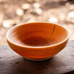 A handcrafted wooden bowl with a smooth, natural finish resting on a wooden surface, showcasing the craftsmanship of green woodworking.